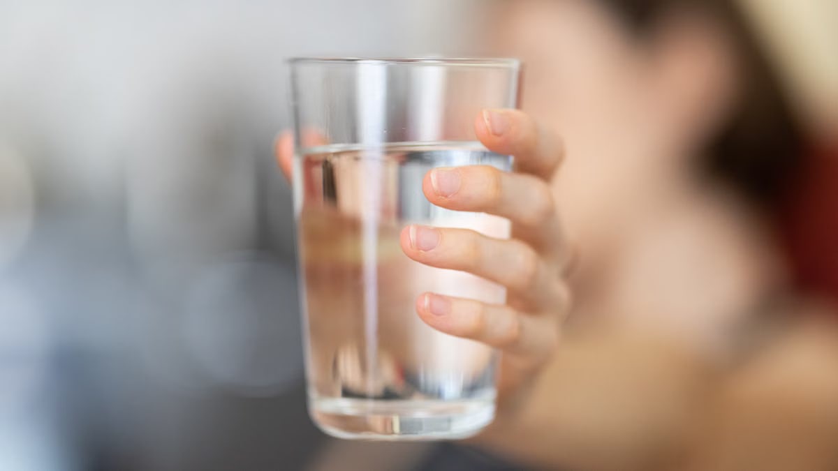 A hand holding a clear glass of water with a blurred background for health and hydration concept.